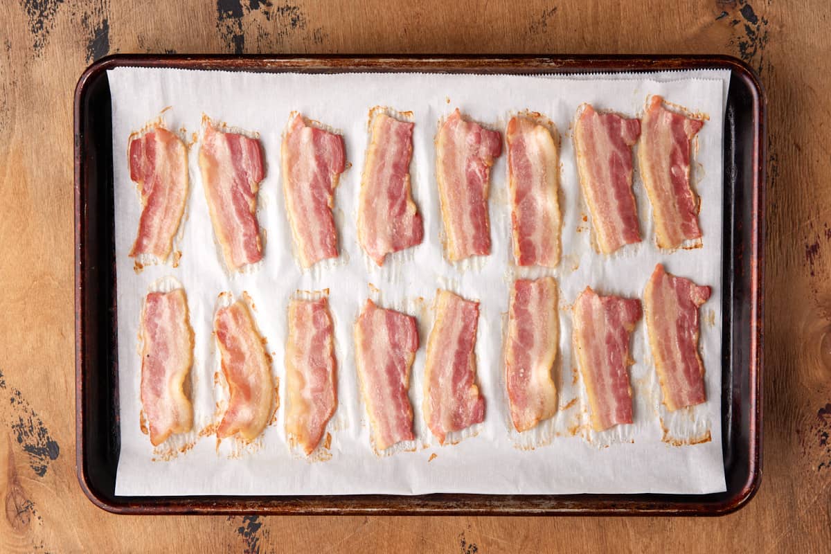 Par-baked bacon slices on a sheet pan lined with parchment paper. 