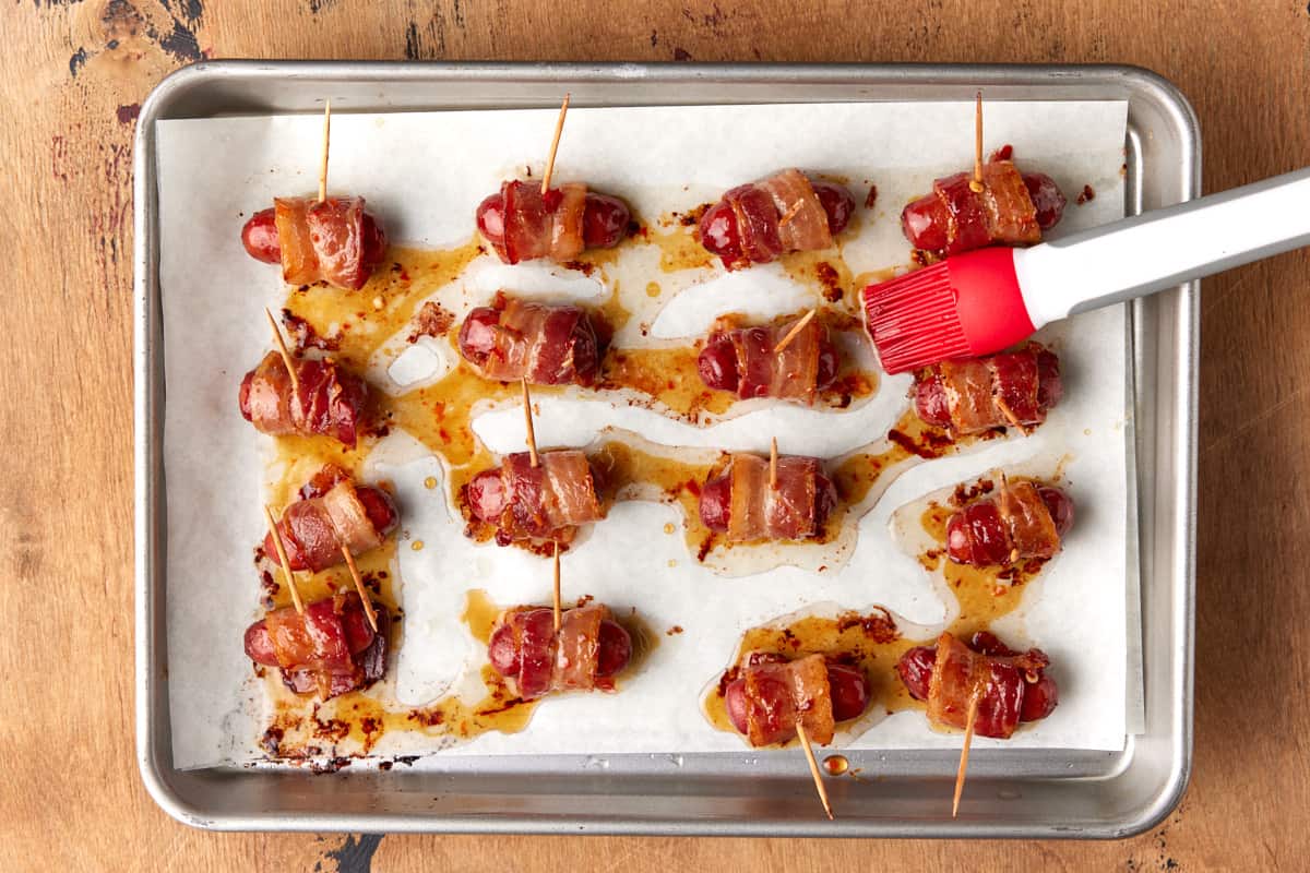 Bacon wrapped smokies brushed with sauce on sheet pan. 