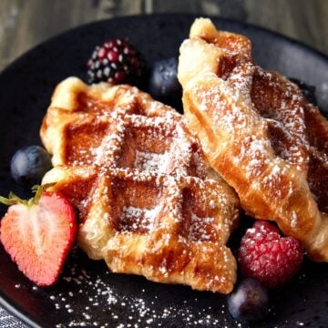 Two croffles on a dark plate with powdered sugar and berries.