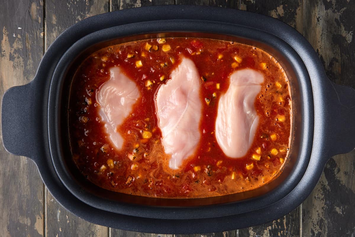 raw chicken breasts in slow cooker with soup ingredients.