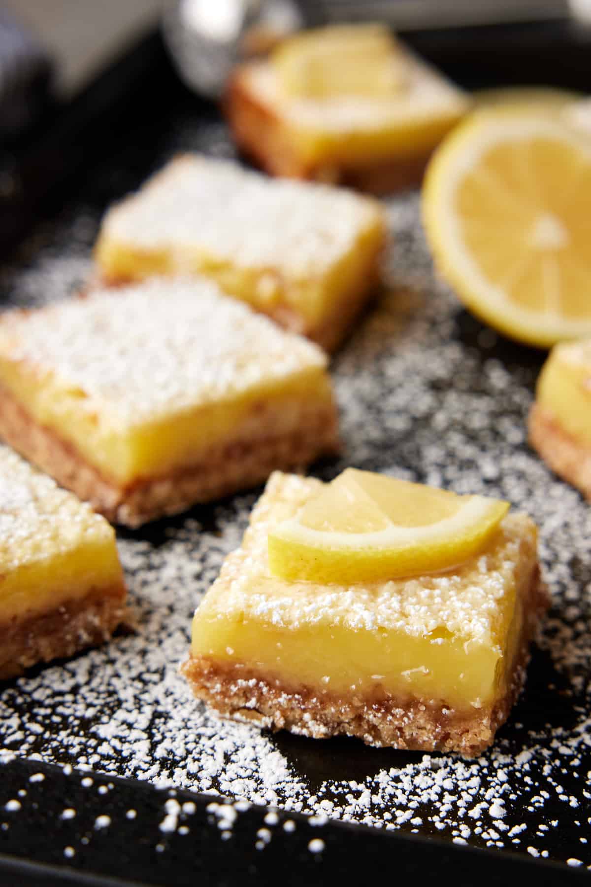 Close up shot of coconut lemon bar dusted with powdered sugar on dark sheet pan. 