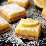 Coconut lemon bars dusted with powdered sugar on dark sheet pan.