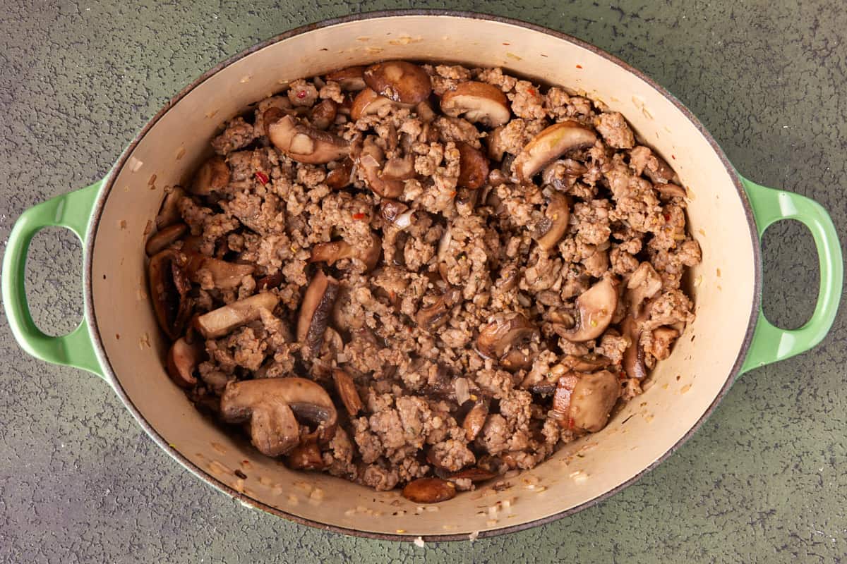 Dutch oven with browned sausage, mushrooms and shallots. 