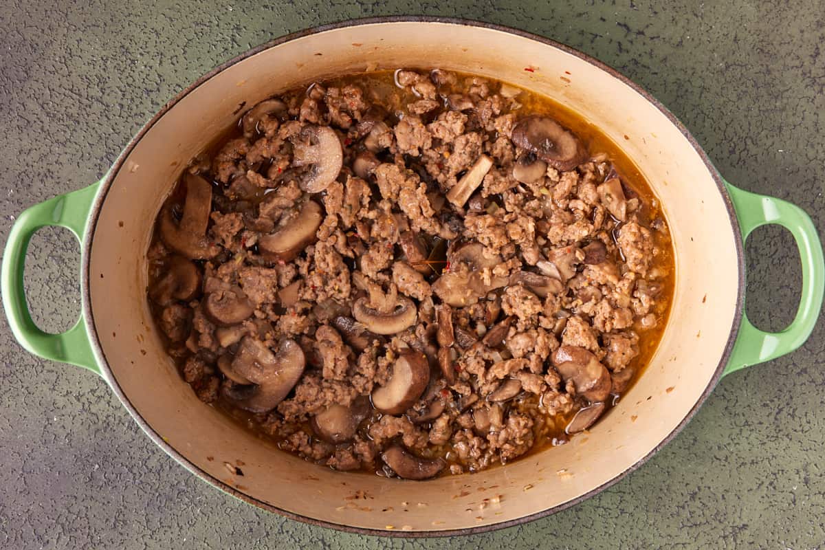 Dutch oven with browned sausage, mushrooms and shallots and reduced wine sauce. 