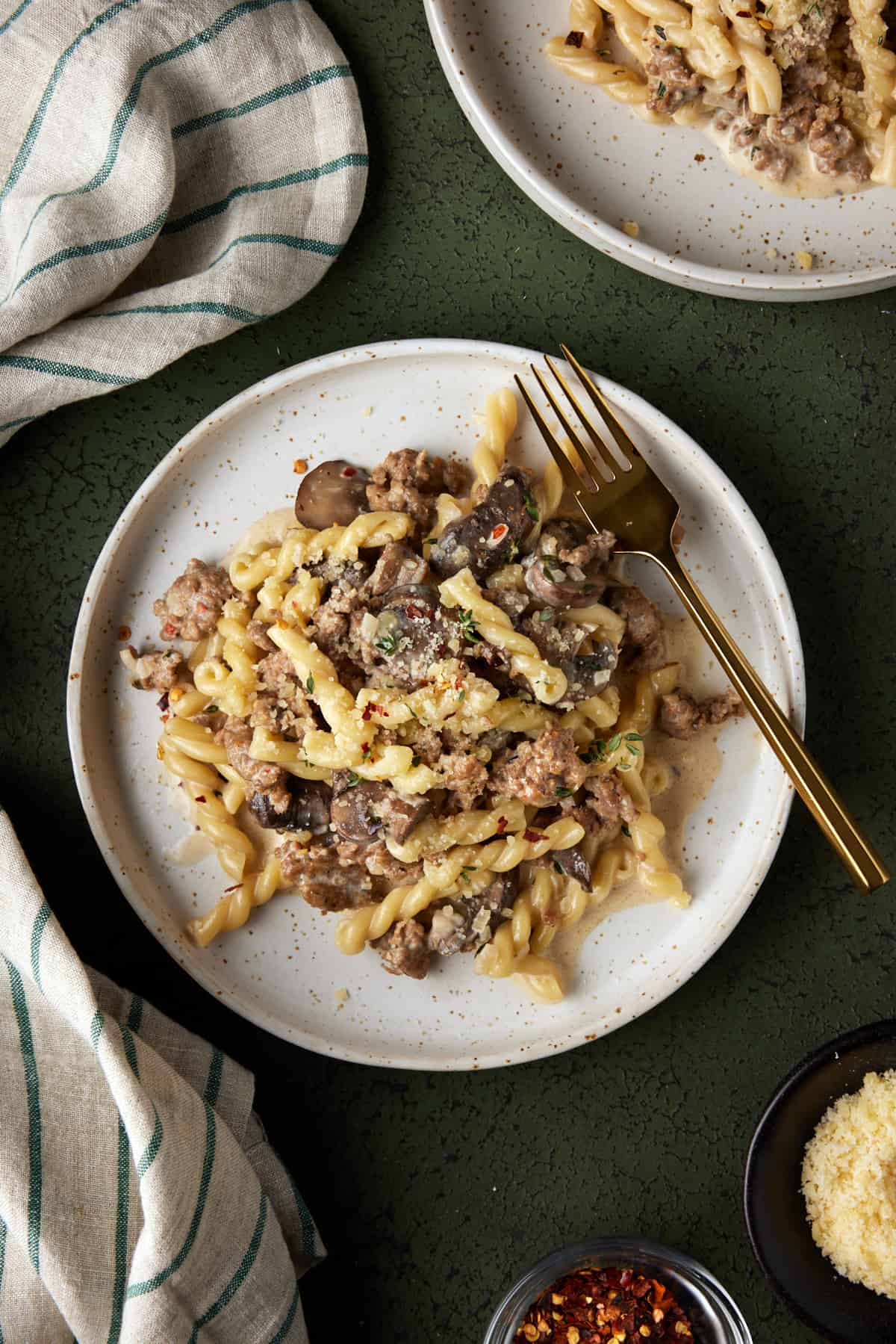 Two cream plates of creamy sausage and mushroom pasta. 