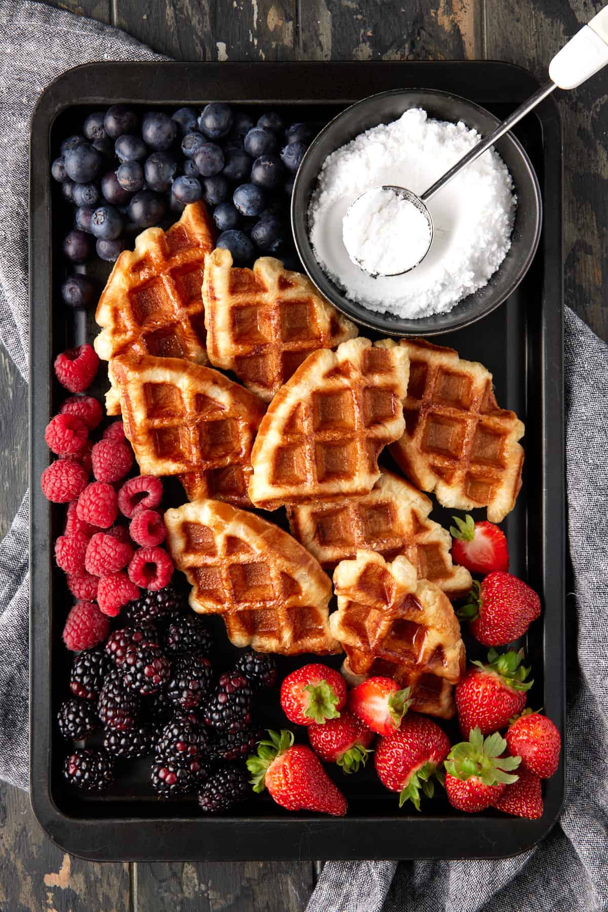 Croffles on a dark sheet pan with fruit and powdered sugar. 