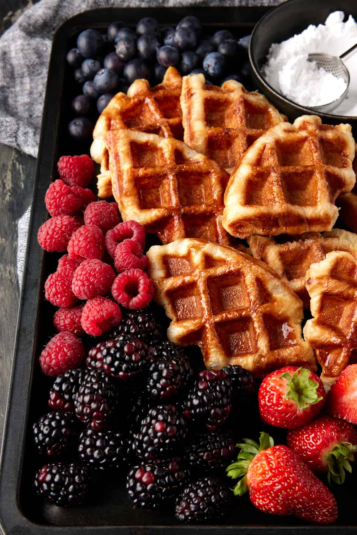 Baked croffles on a sheet pan with berries and powdered sugar. 