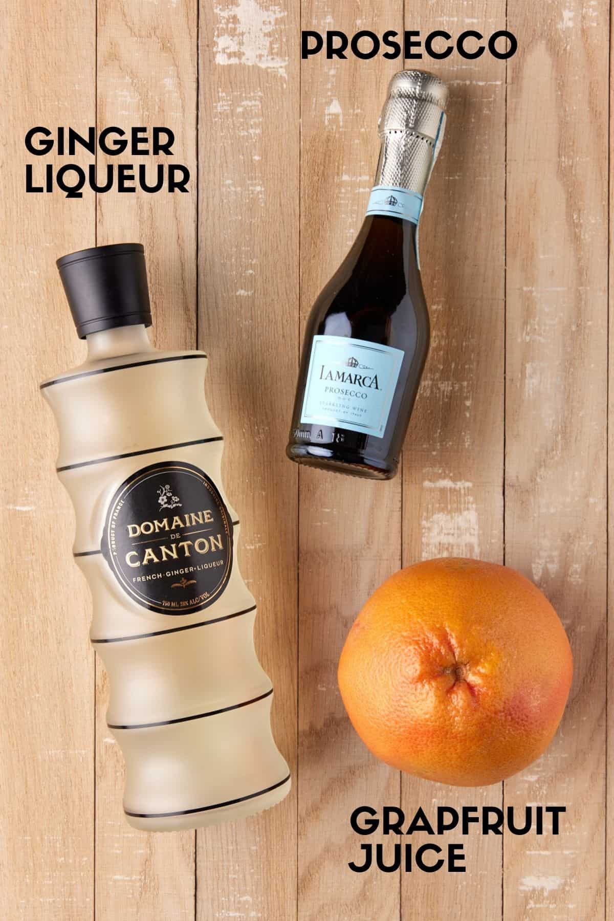 Bottles of prosecco, ginger liqueur and a grapefruit on a light wood board. 