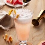 Sparkling wine being poured into fluted glass with grapefruit juice.