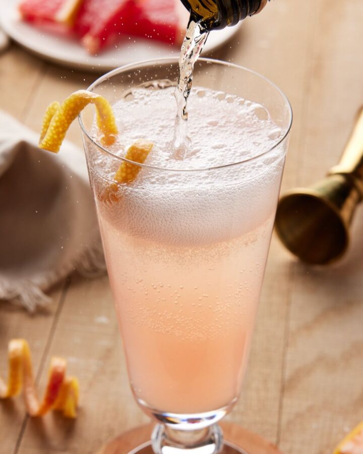 Sparkling wine being poured into fluted glass with grapefruit juice.