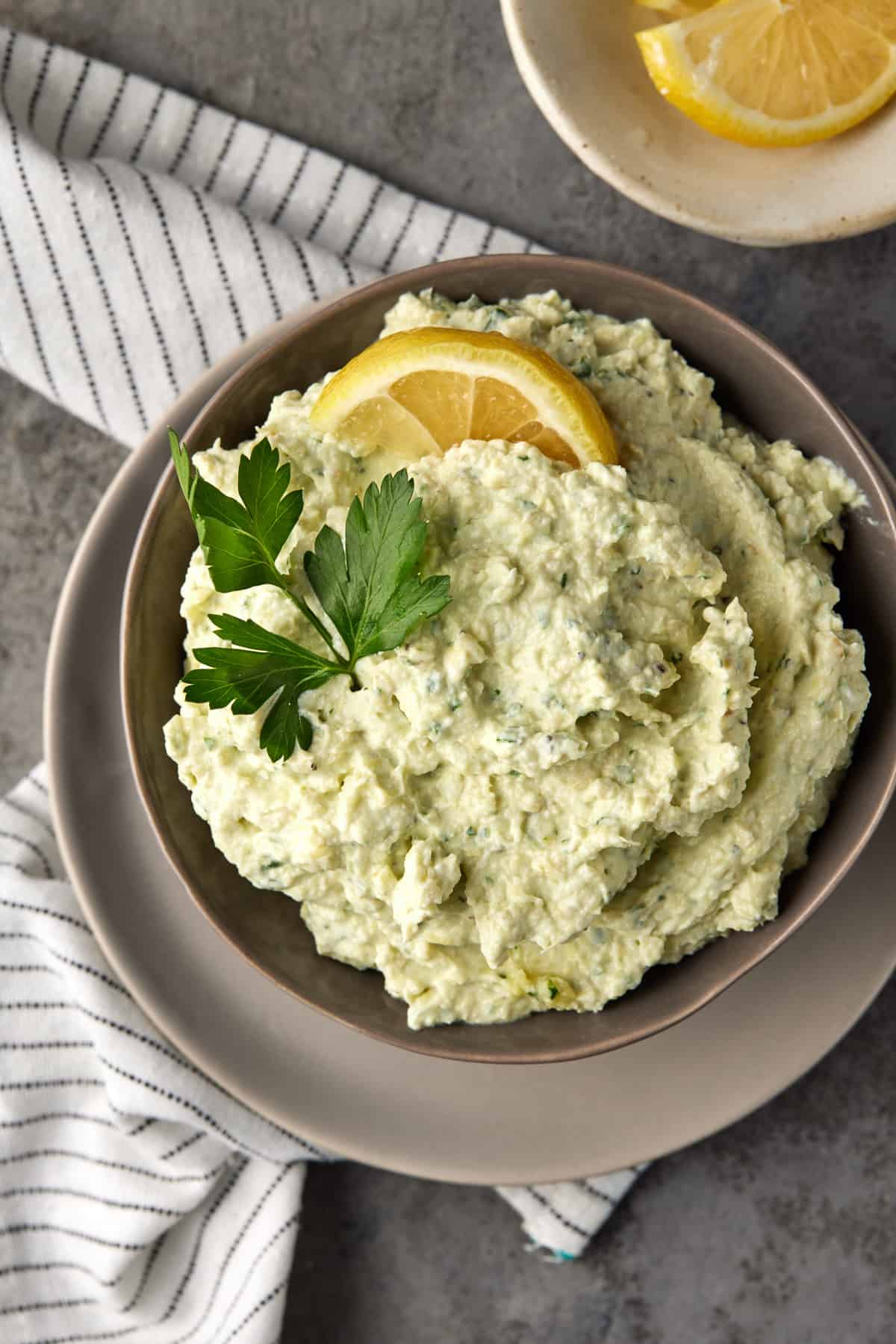 Artichoke dip in a bowl with lemon and parsley.