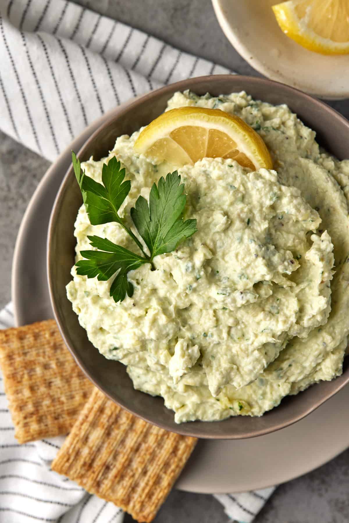 Bowl filled with artichoke dip and garnished with lemon and parsley.