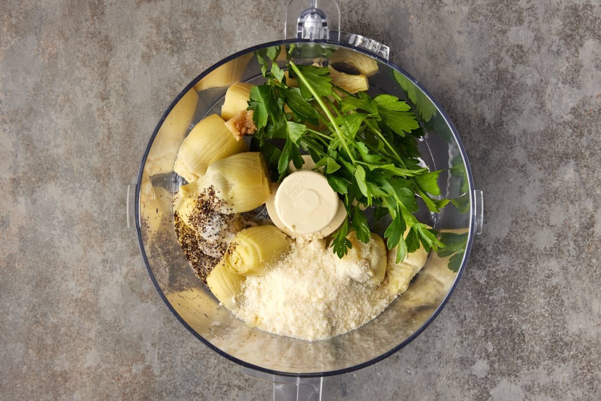 Food processor filled with artichokes, parmesan cheese and parsley.