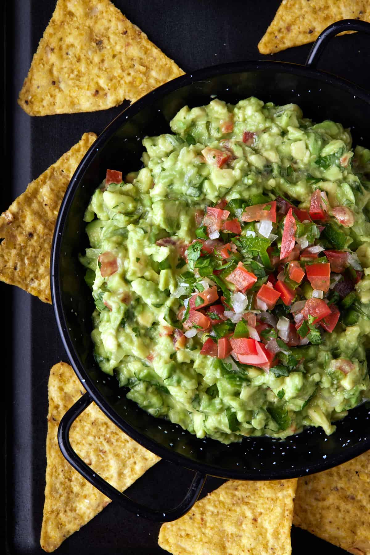 Black metal bowl filled with chunky guacamole and topped with pico de gallo. 