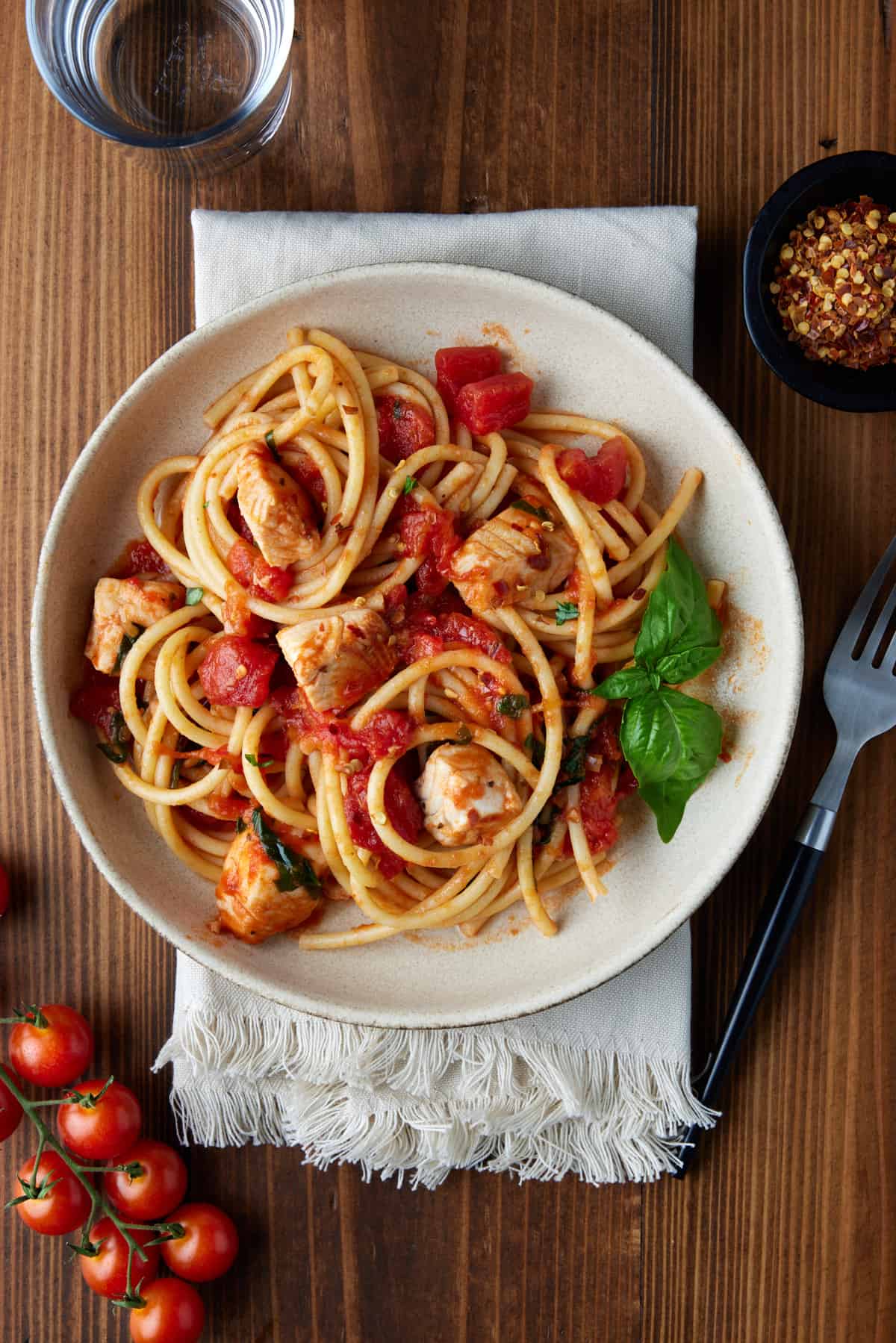 Tilapia with tomatoes and pasta in a bowl with crushed red pepper.