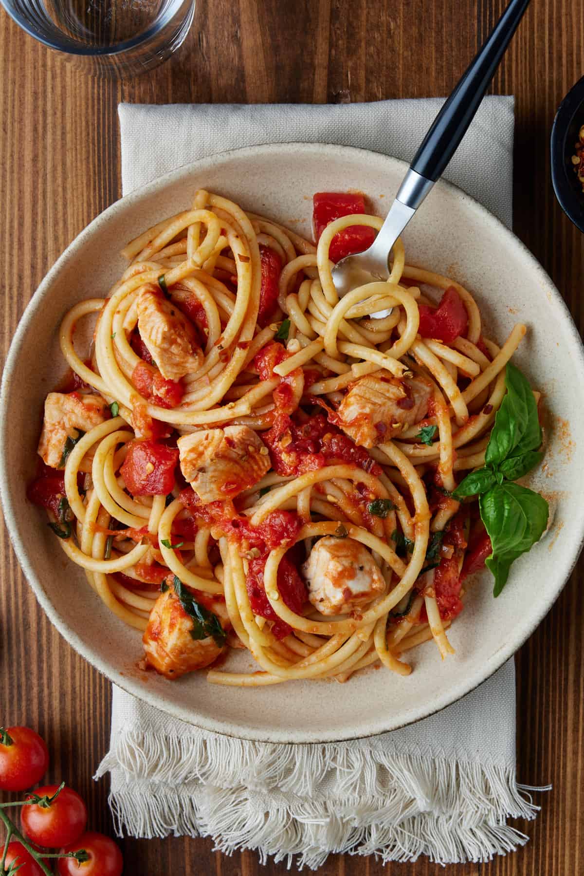 Pasta twirled around a fork with tilapia and tomatoes.