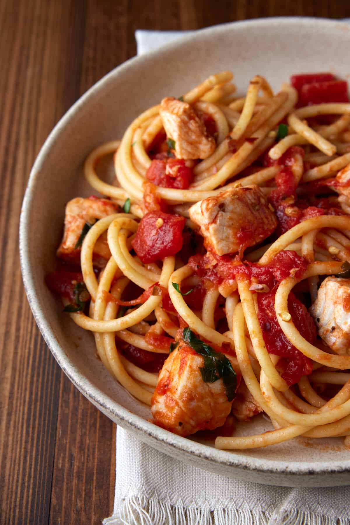 Cooked tilapia with tomato sauce, crushed red pepper and pasta in a bowl.