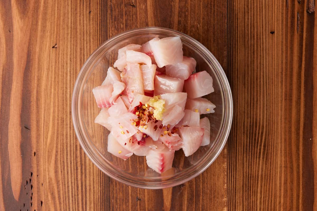 Tilapia chunks in bowl with garlic and olive oil.