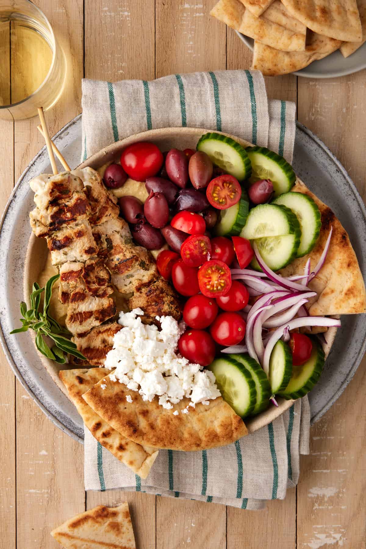 Chicken Souvlaki in a bowl with pita, fresh veggies and feta cheese.