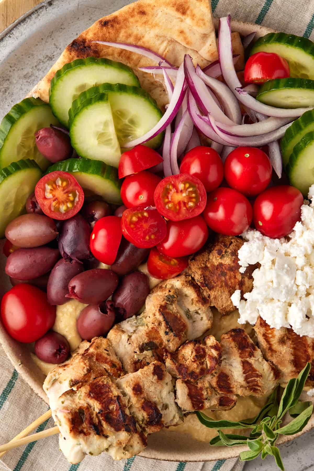 Chicken skewers in bowl with pita, olives, tomatoes, cucumber and feta cheese.