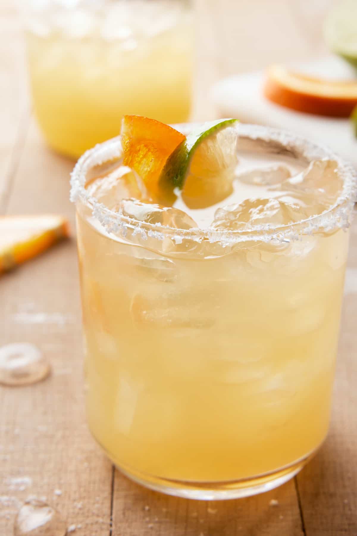 Salt rimmed glass filled with Italian Margarita and garnished with orange and lime, with shaker in back.