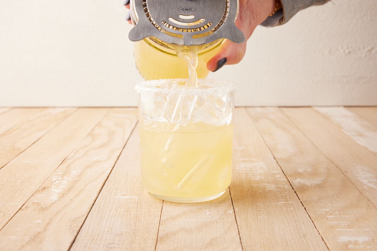 Shaker pouring drink into salt rimmed glass.
