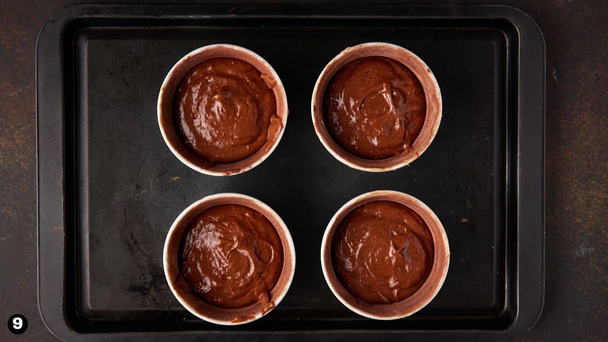 Ramekins filled with chocolate cake batter on sheet pan. 