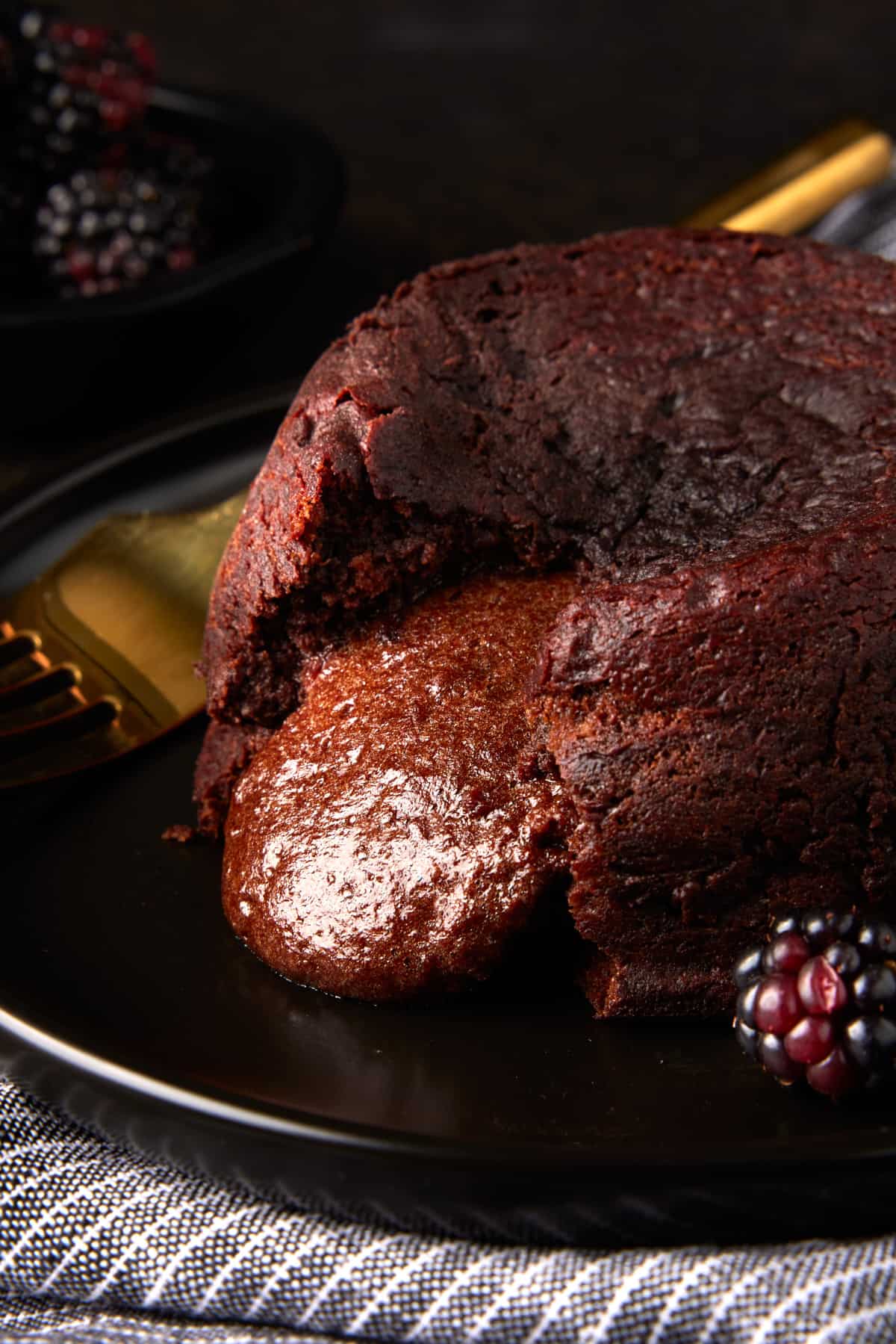 Molten chocolate filling oozing out of chocolate cake on dark plate. 