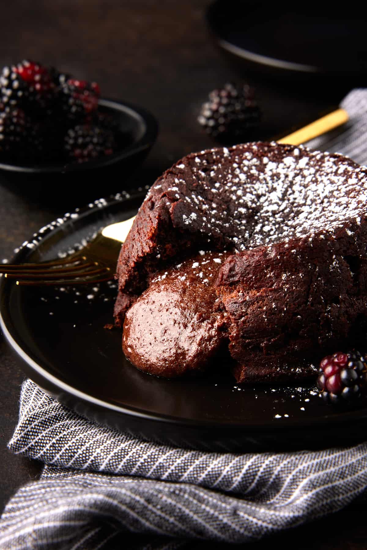 Molten chocolate lava cake on black plate with liquid center oozing out. 