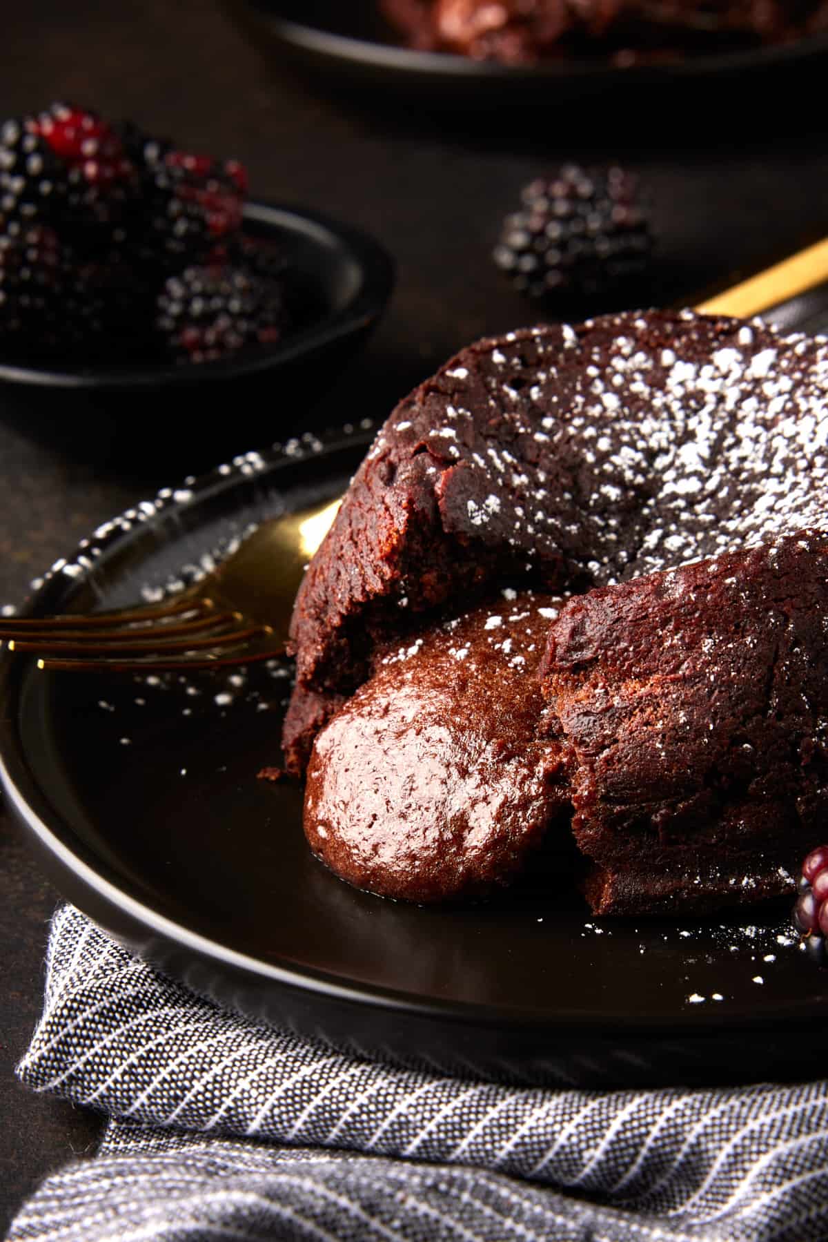 Molten chocolate lava cake with oozing center and powdered sugar on dark plate. 