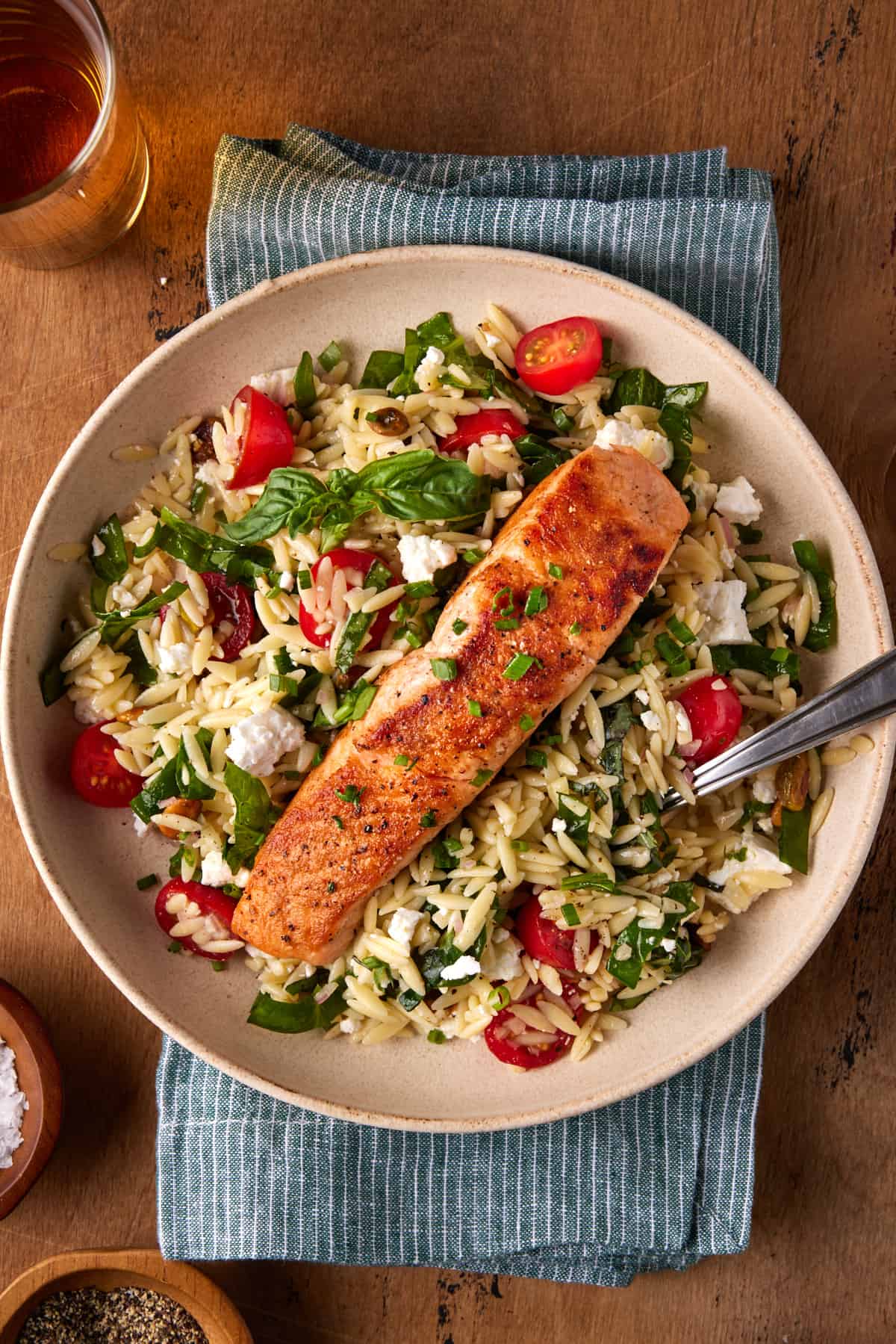 Seared salon on an orzo salad in a bowl with a fork. 