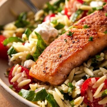 Seared salmon filet on top of orzo salad in a bowl.