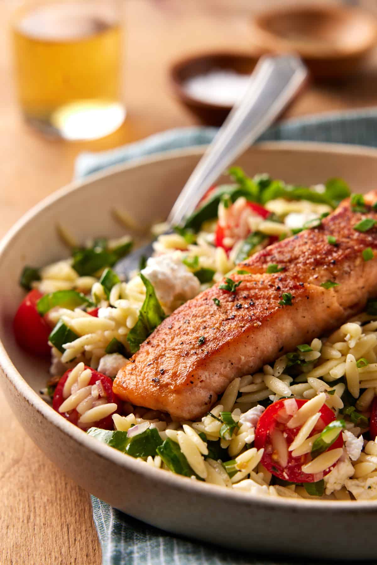 Seared salmon filet in a bowl with orzo salad and a fork. 
