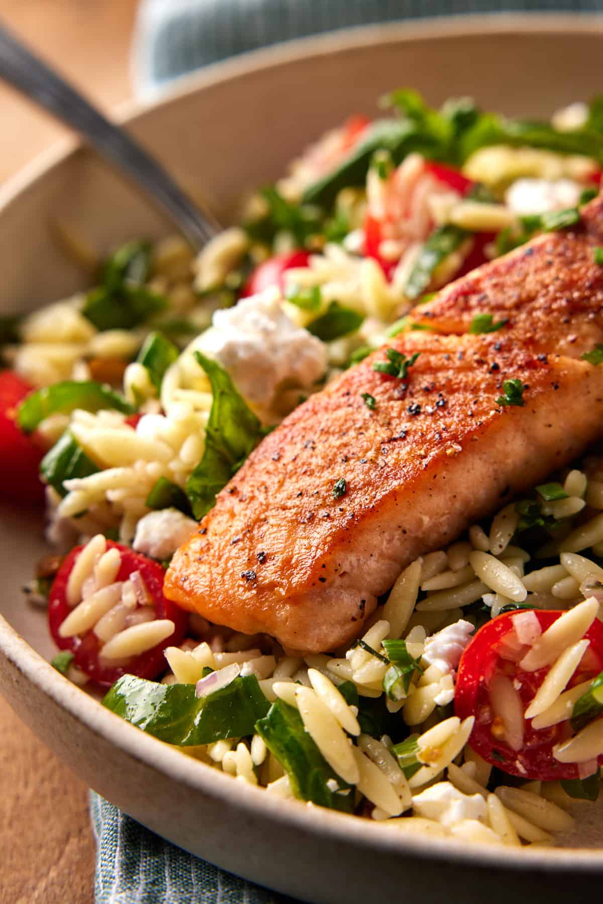 Seared salmon in a bowl of orzo salad with a fork. 