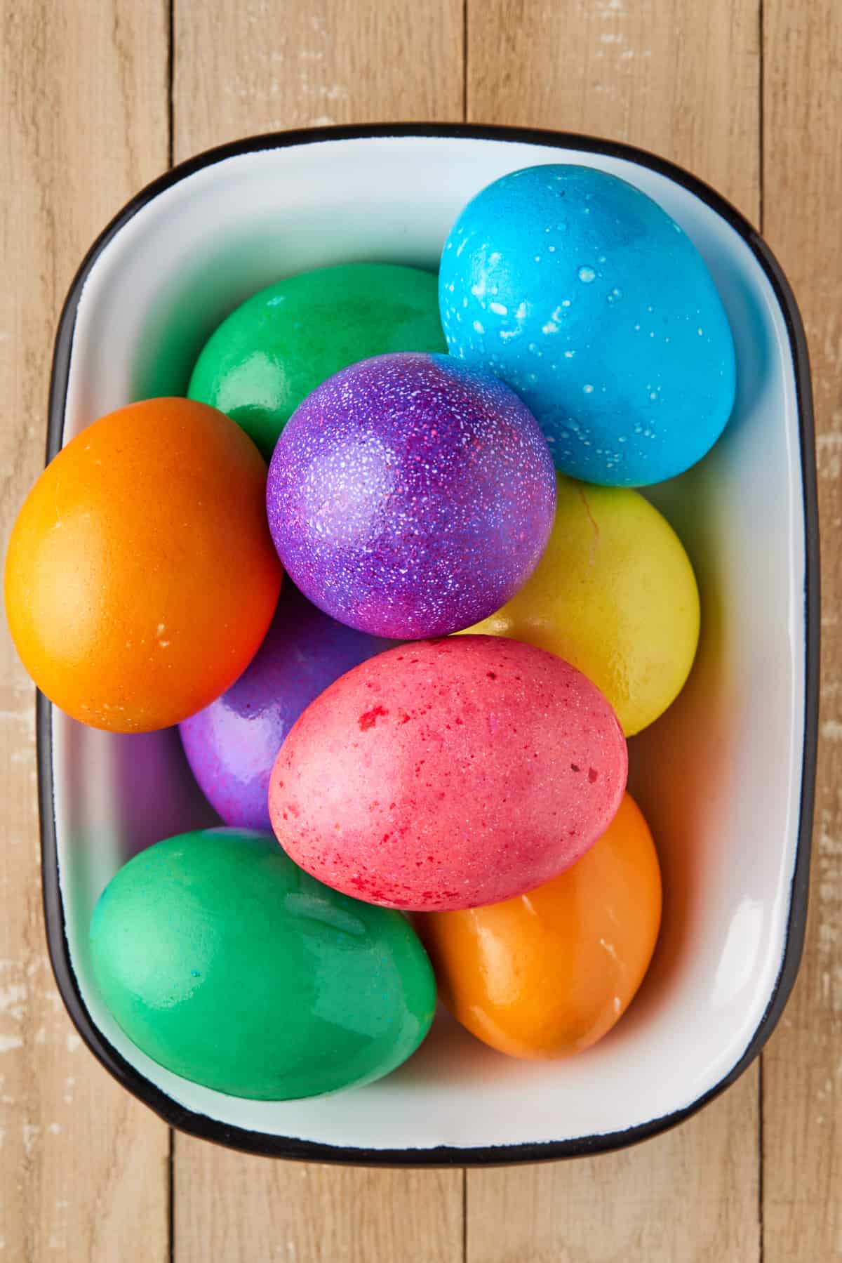 Colored hard boiled eggs in white dish.