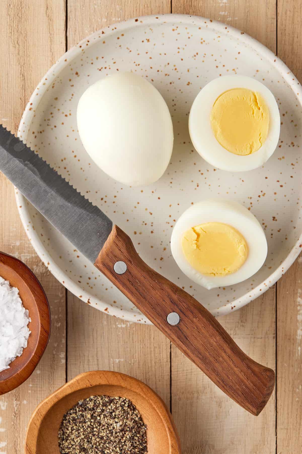 Sliced hard boiled egg with knife and salt and pepper.