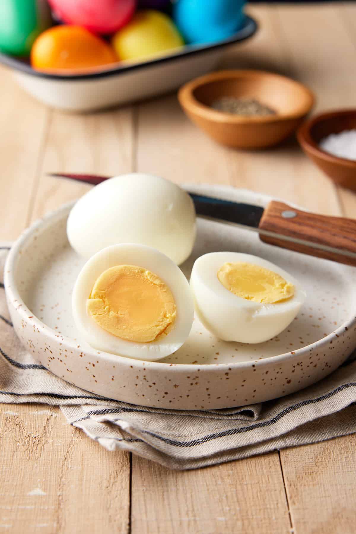 Sliced hard boiled egg on plate with knife and salt and pepper.