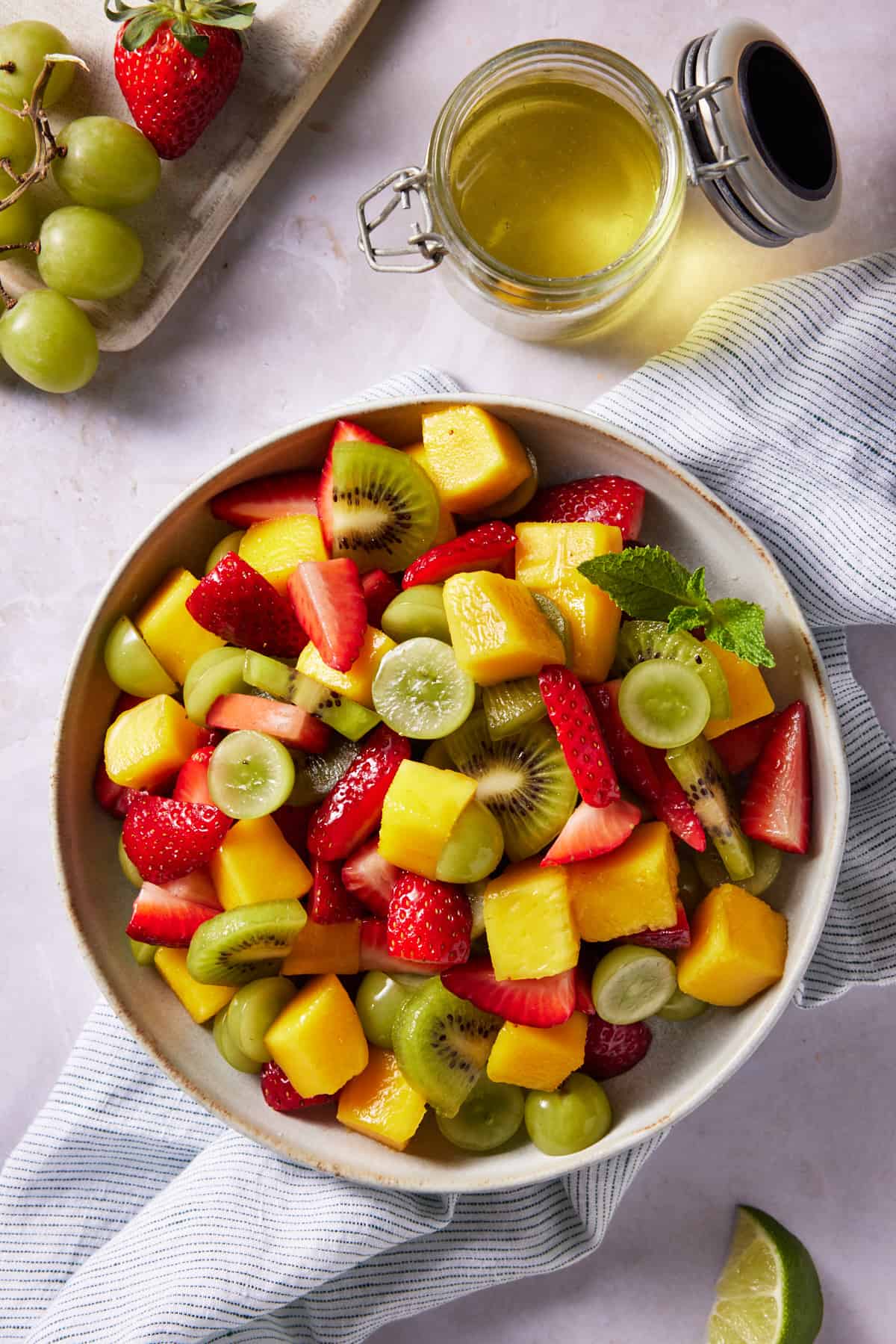 Fruit salad in a cream bowl next to a glass jar of fruit salad dressing. 