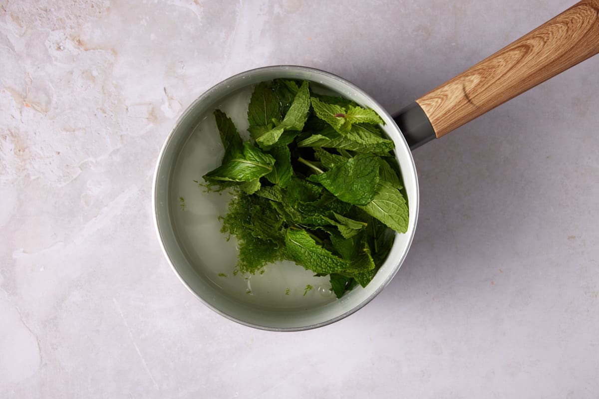 Mint and lime zest added to simple syrup in a white saucepan. 