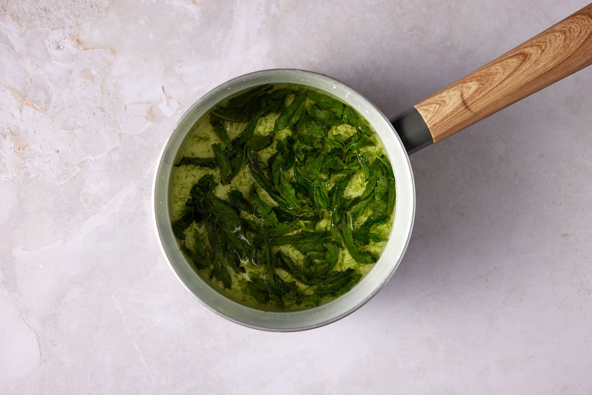 Mint and lime zest stirred into warm simple syrup in a white saucepan. 