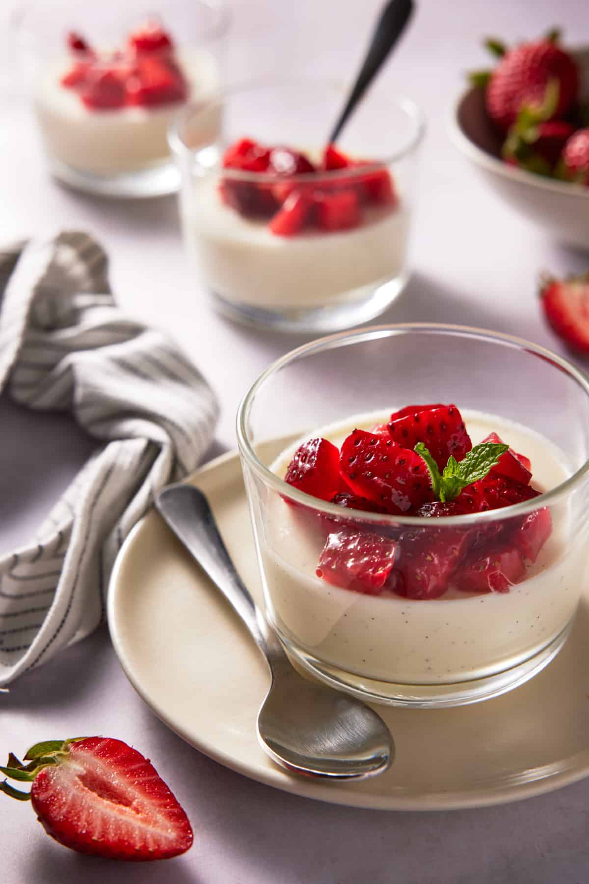 Vanilla bean panna cotta in a glass ramekin on a cream plate. Topped with strawberries. 