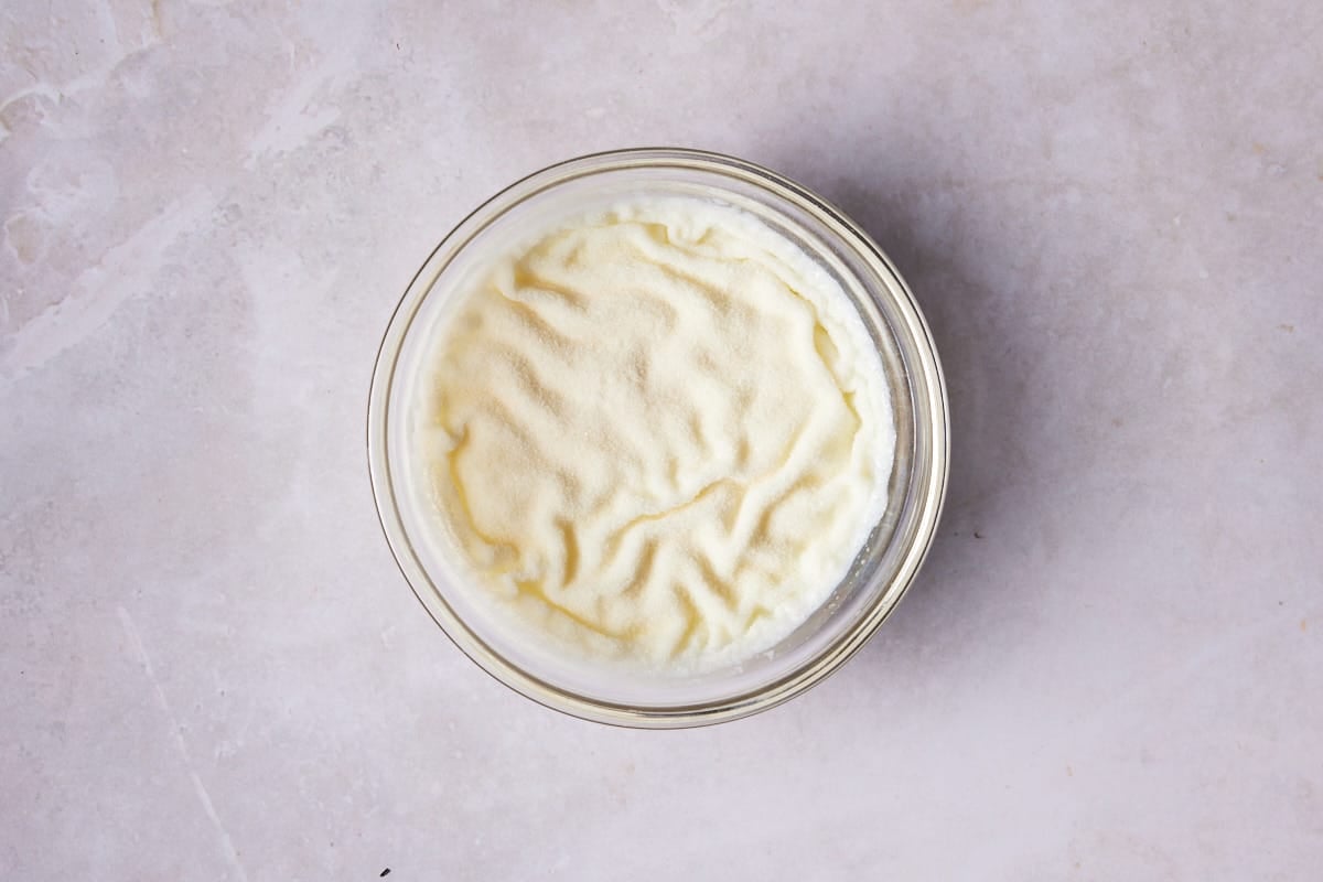 Gelatin sprinkled on top of milk in a glass bowl. 