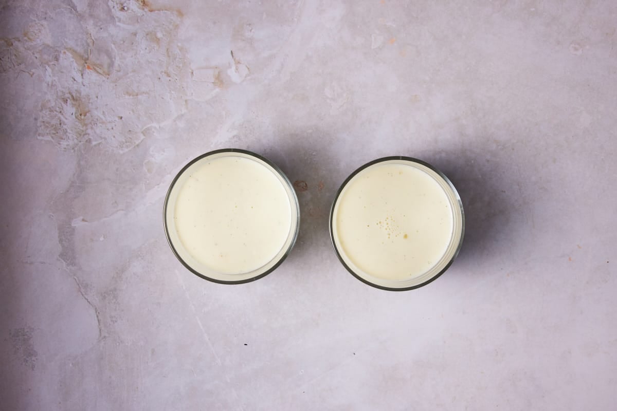 Two glass ramekins filled with vanilla bean panna cotta mixture. 