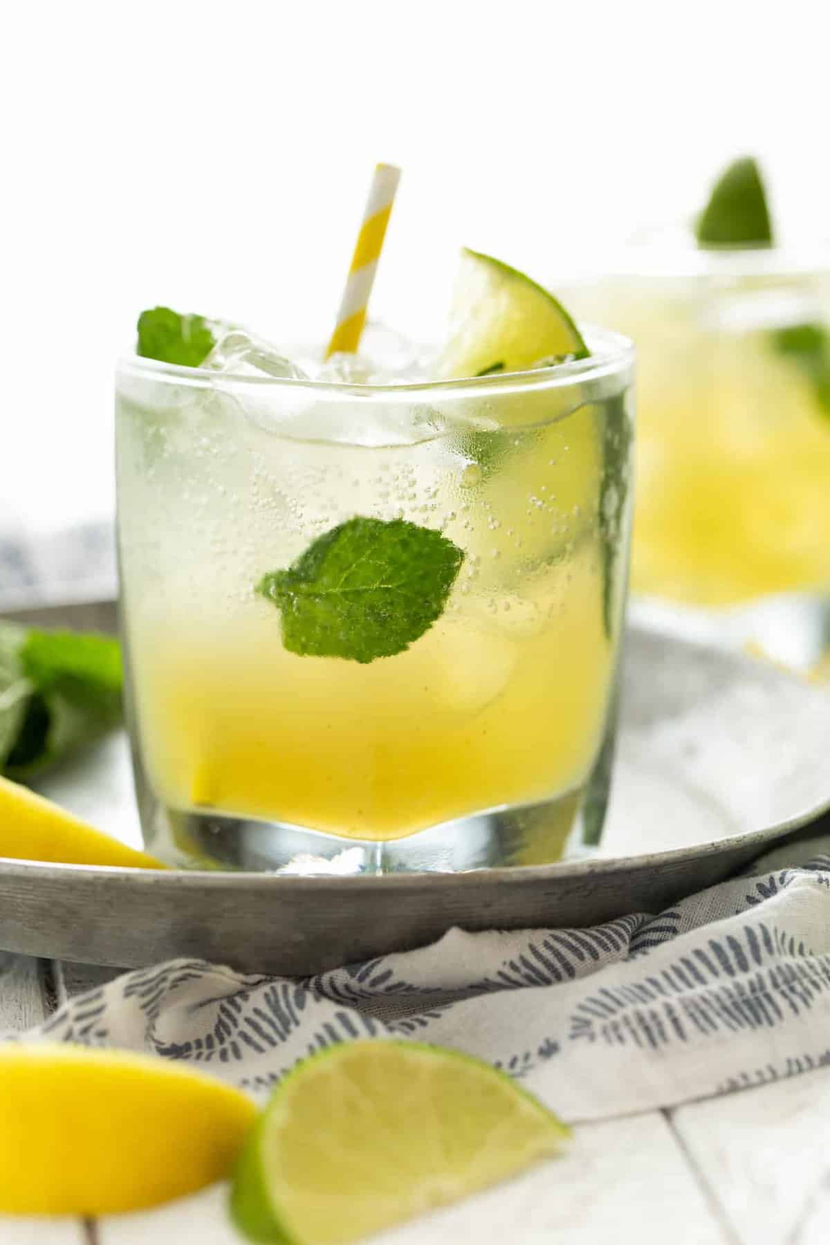 close up: low ball glass filled with ice and mint leaves and bootleg cocktails on a silver tray with a yellow straw