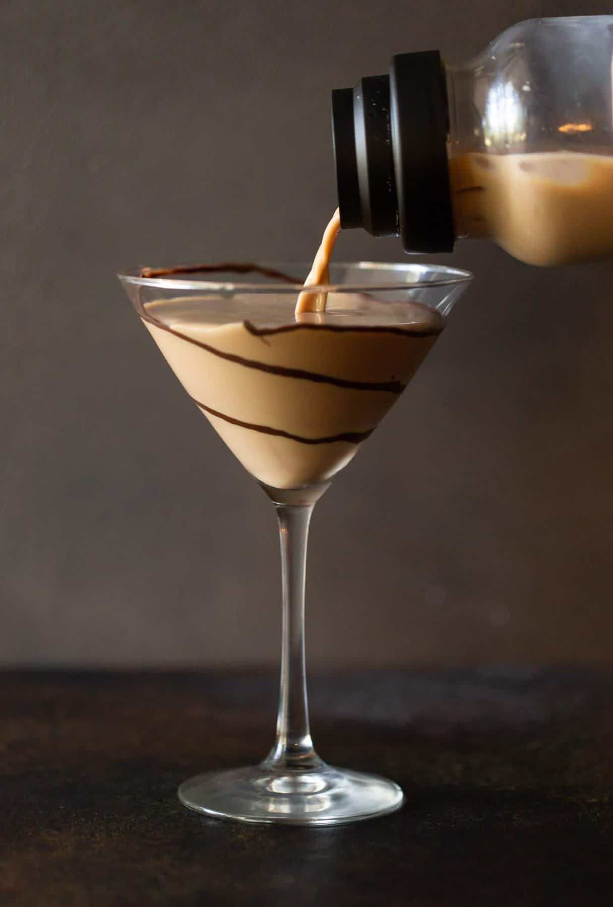 Clear shaker pouring chocolate martini into tall glass with chocolate swirls.