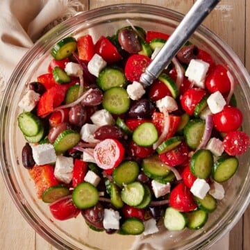 Glass bowl filled with cucumbers, tomatoes, olives and feta cheese.