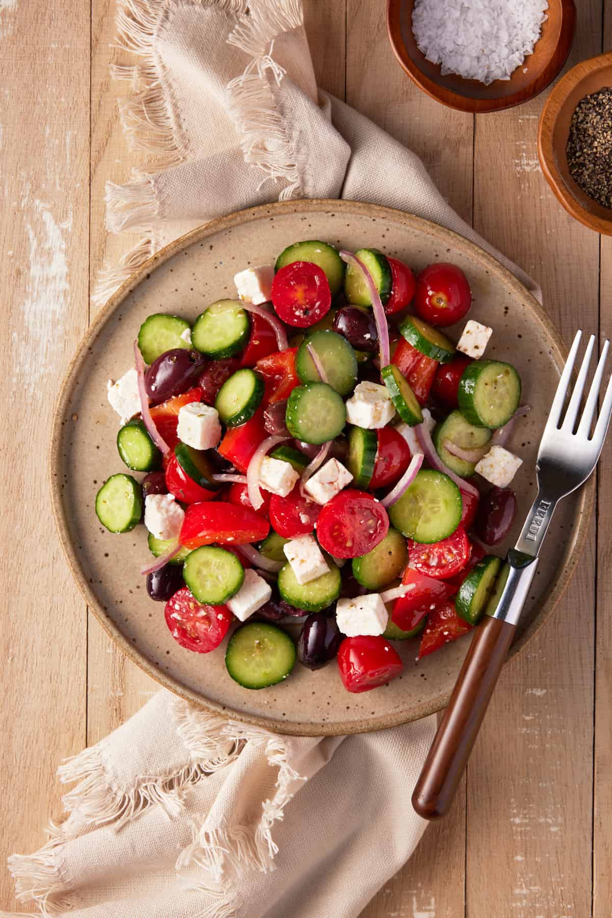 Greek cucumber salad on a speckled beige plate with a fork and beige linen. 