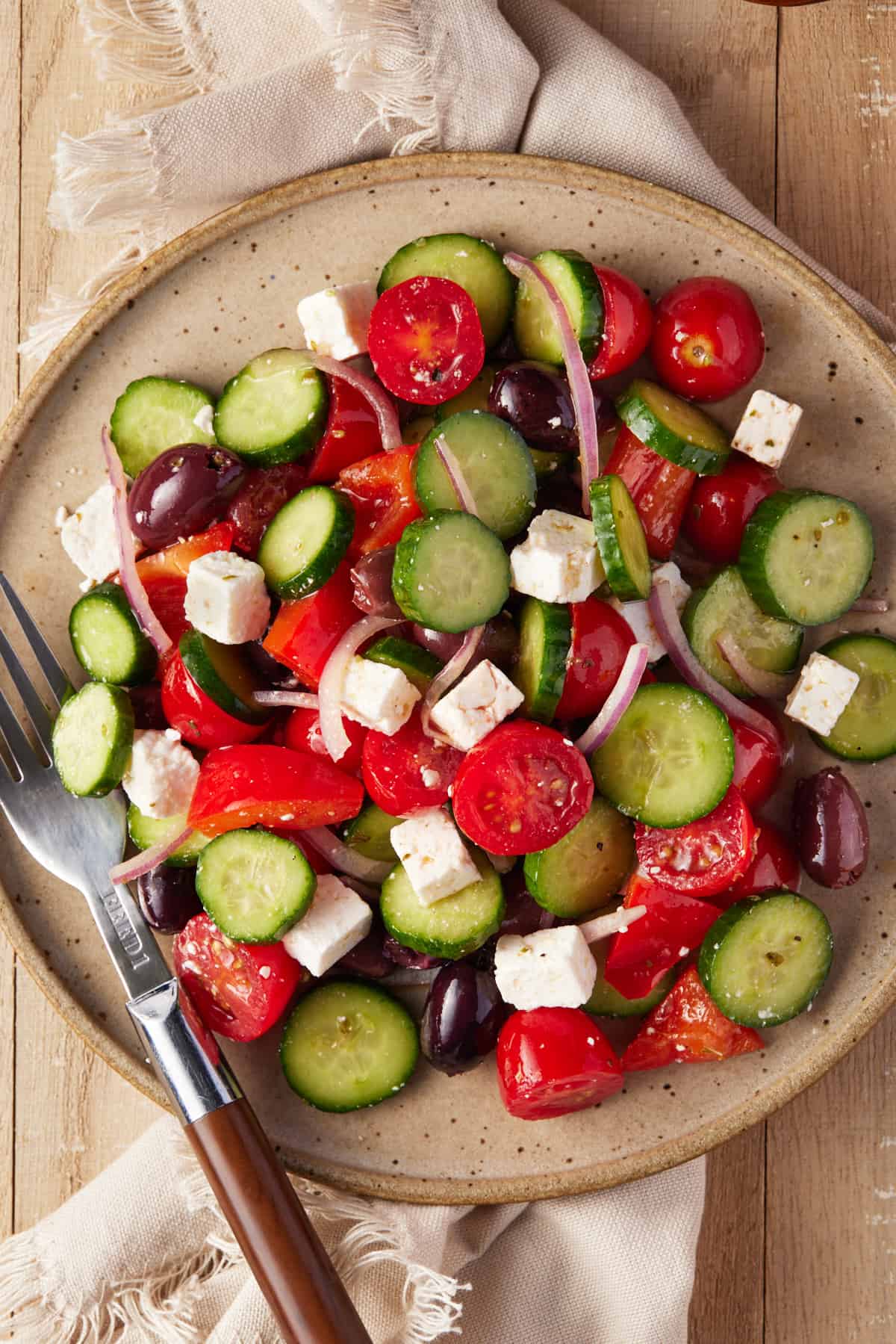 Greek cucumber and tomato salad on a beige pottery plate with a fork. 