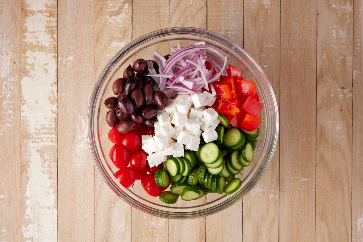Cucumbers, tomatoes, olives, feta cheese, bell pepper and red onion in a glass bowl. 