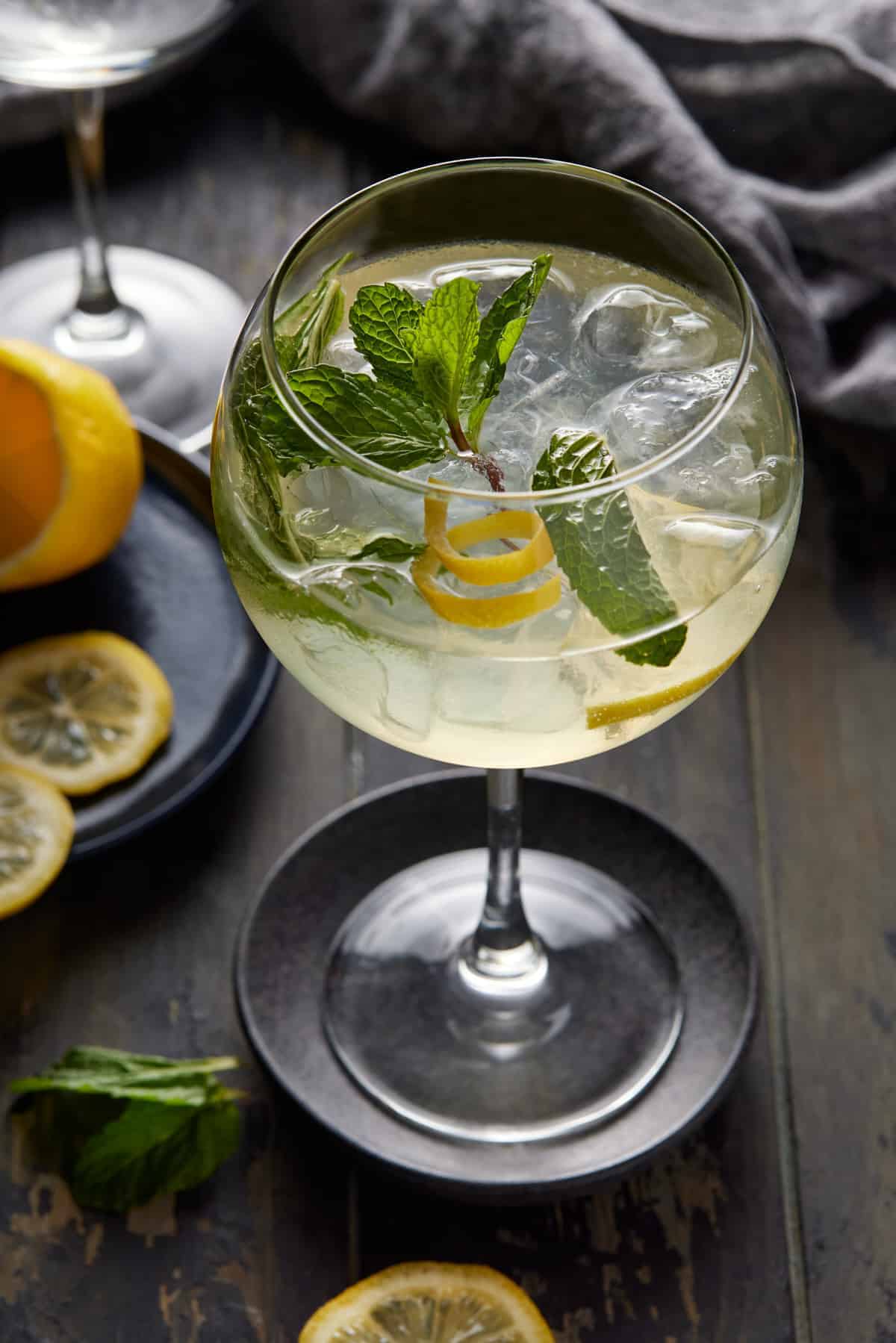 Hugo spritz cocktail in an ice-filled wine glass garnished with lemon and mint.